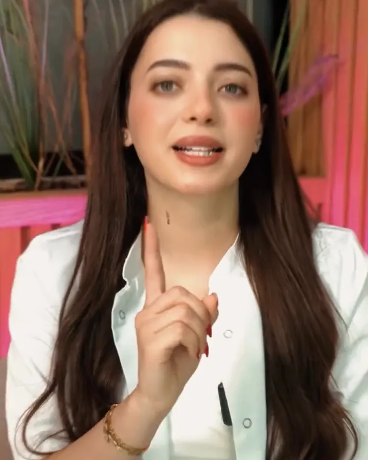 La fondatrice en blouse blanche, l'index levé, face caméra